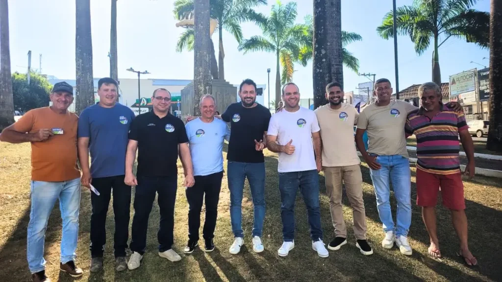 Grupo de homens posa para foto ao ar livre em área com palmeiras